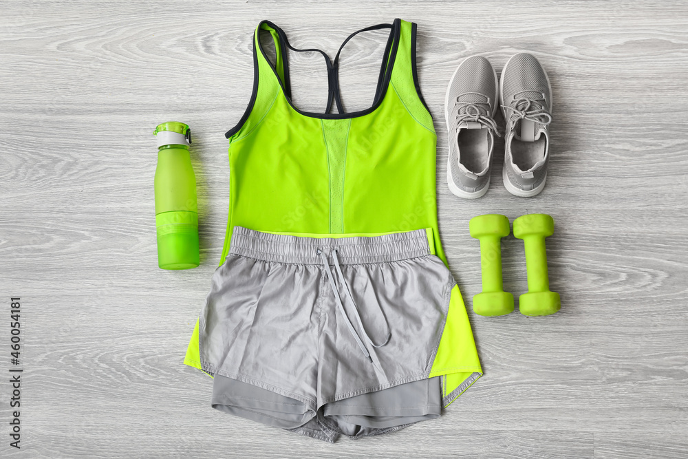 浅色木质背景上的运动服、鞋、哑铃和水瓶
