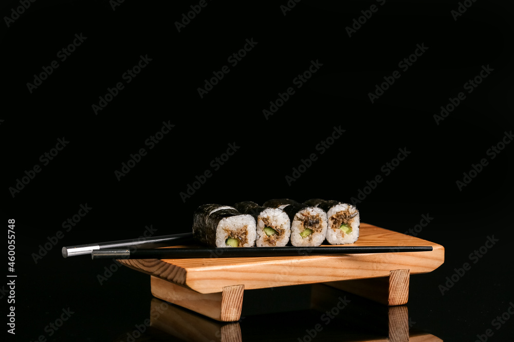 深色背景下有美味寿司卷和筷子的木板