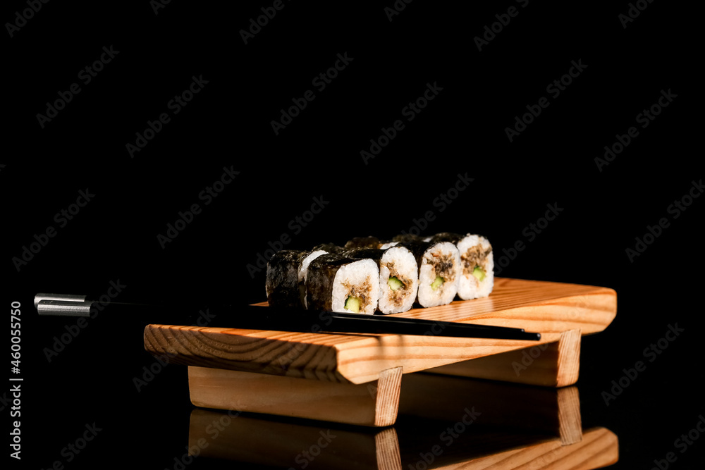 Wooden board with tasty sushi rolls and chopsticks on dark background