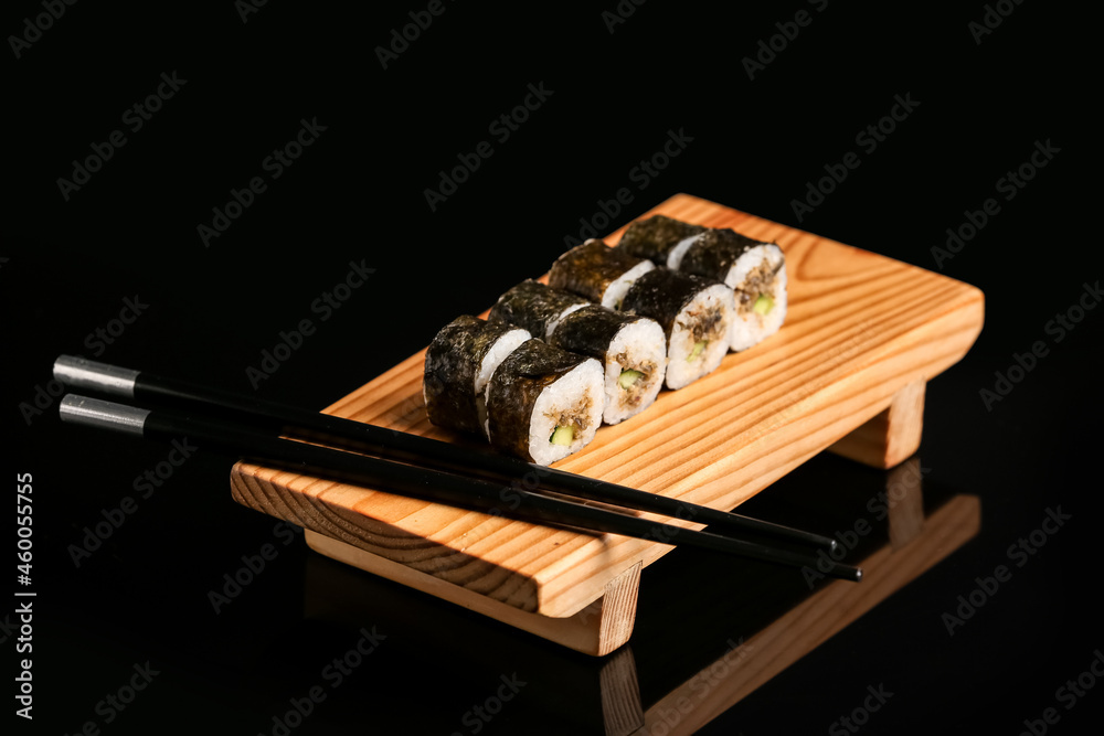 Wooden board with tasty sushi rolls and chopsticks on dark background