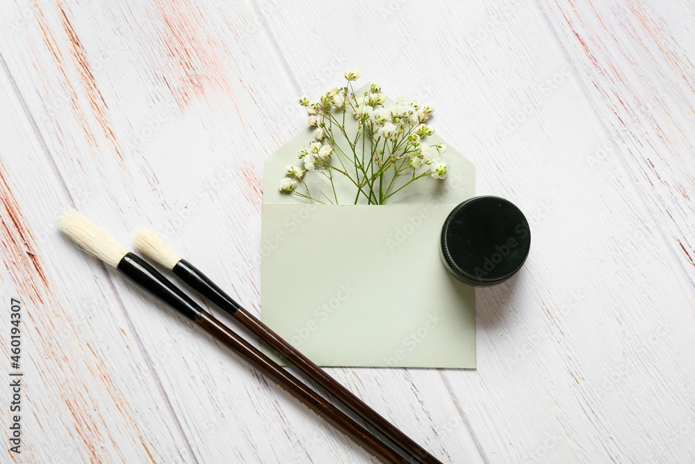 浅色木质背景上的带花朵、墨水和画笔的信封