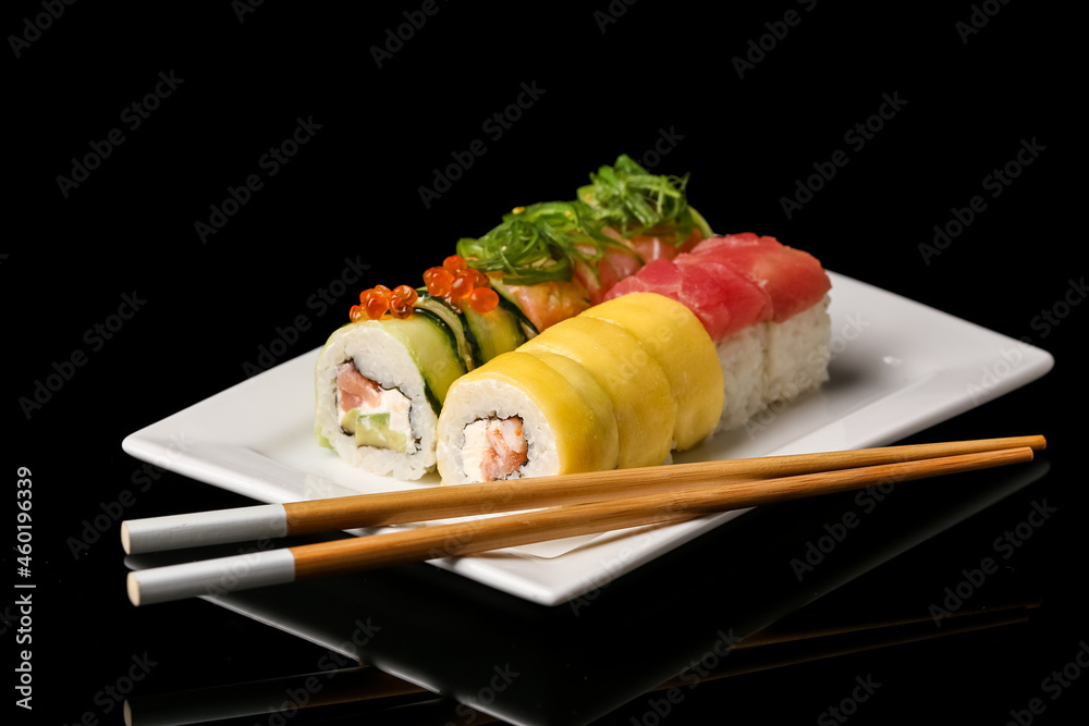 黑色背景上有美味的寿司卷和筷子的盘子