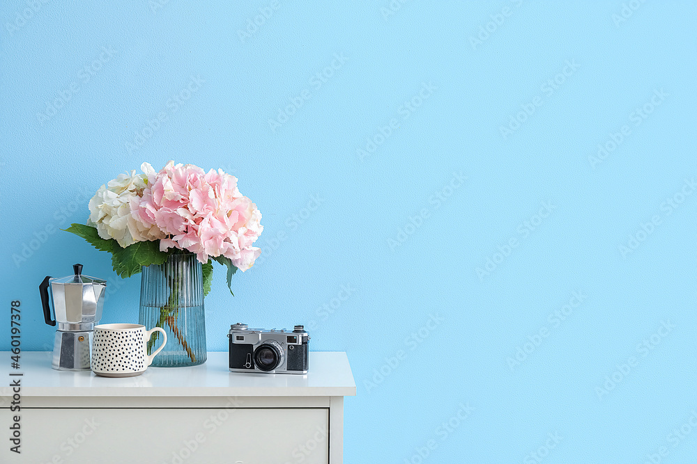 彩色墙壁附近的架子上有绣球花、杯子和照相机的花瓶