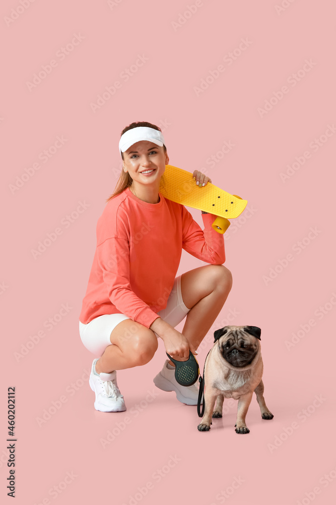 Young woman with skateboard and cute pug dog on pink background