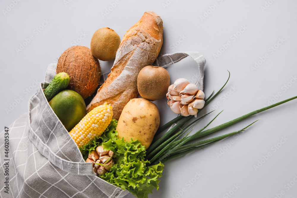 浅色背景下有水果、蔬菜、绿色蔬菜和面包的环保袋，特写