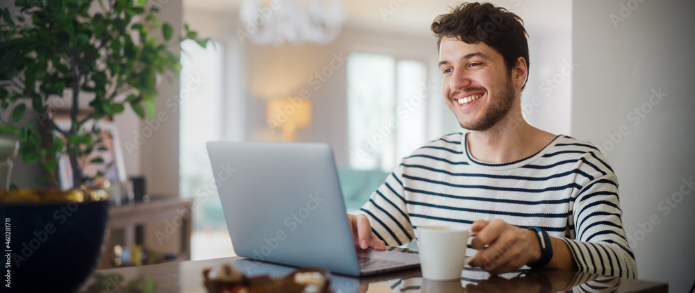 Handsome Adult Man Using Laptop Computer, Sitting in Living Room and Drinking Tea or Coffee in Apart