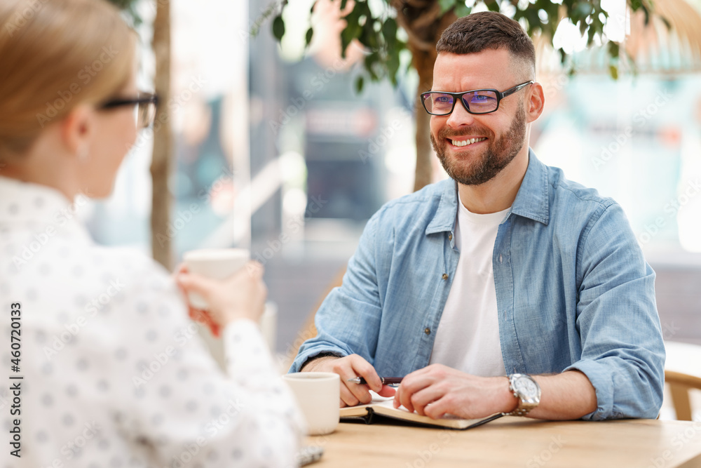 Young cheerful man business professional in eyeglasses at meeting with female client in outdoor cafe