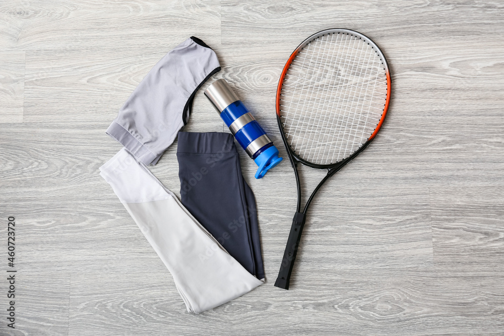 浅色木质背景的运动服、水瓶和网球拍