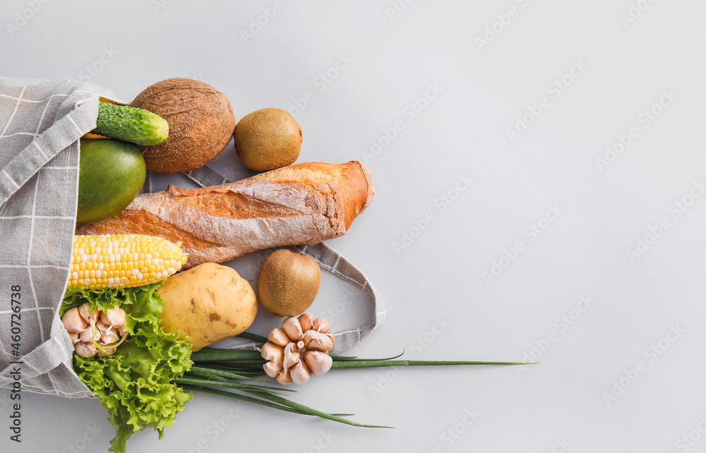 Eco bag with fruits, vegetables, greens and bread on light background