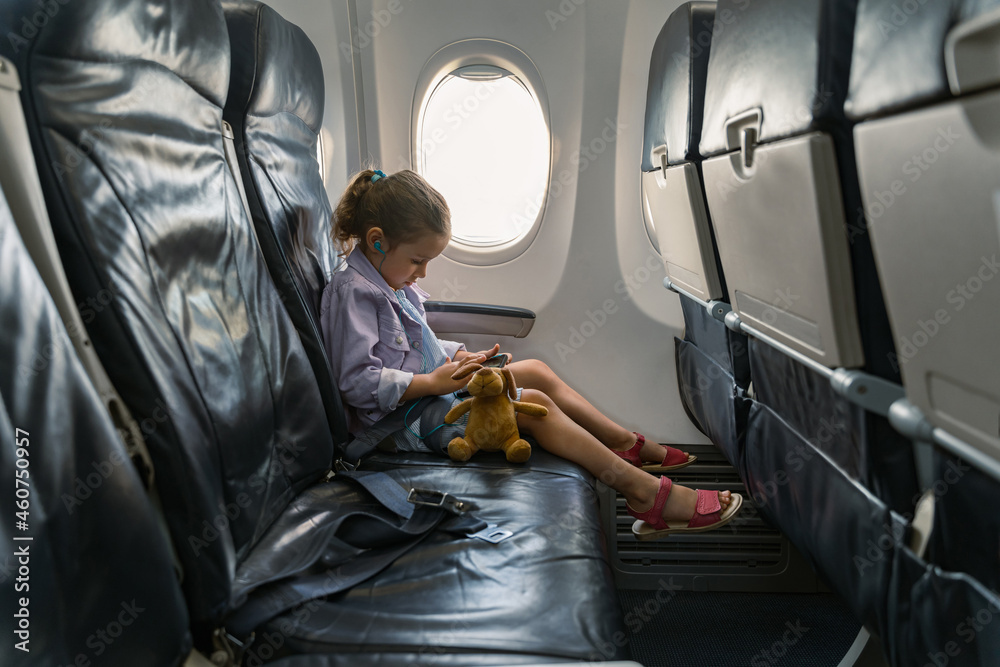 可爱的孩子在飞机上使用耳机时看手机的侧视图。旅行概念