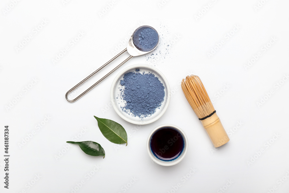 Composition with cup of blue matcha tea, powder and chasen on white background