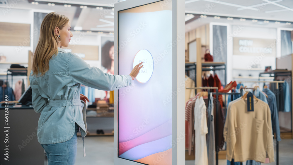 Beautiful Female Customer Using Floor-Standing LCD Touch Display while Shopping in Clothing Store. S