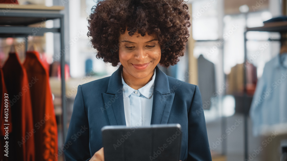 一位快乐的女性营销经理在时尚服装店使用平板电脑的画像。
