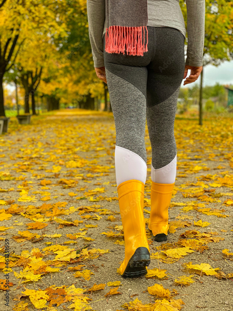 低角度：穿着橡胶靴的女人沿着树叶覆盖的大道行走
