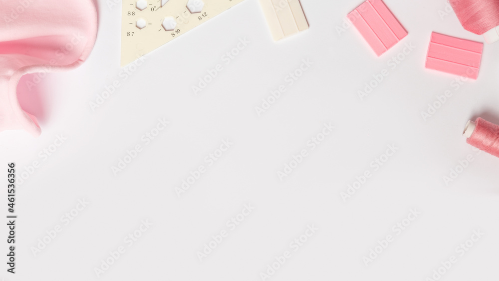 时尚背景。白色桌子上的粉色面料、线和各种设计师配饰，俯视图