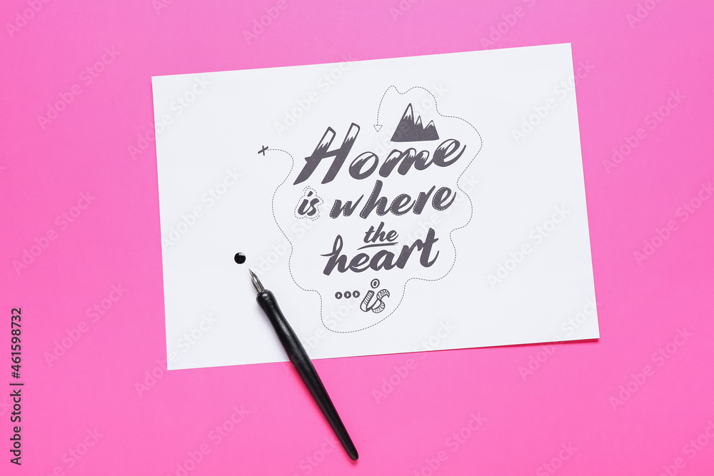 纸上写着家在心在的地方，笔尖在粉色背景上