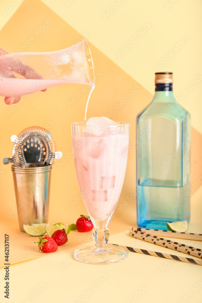 一名女子将草莓Pina Colada鸡尾酒倒入彩色背景的玻璃杯中