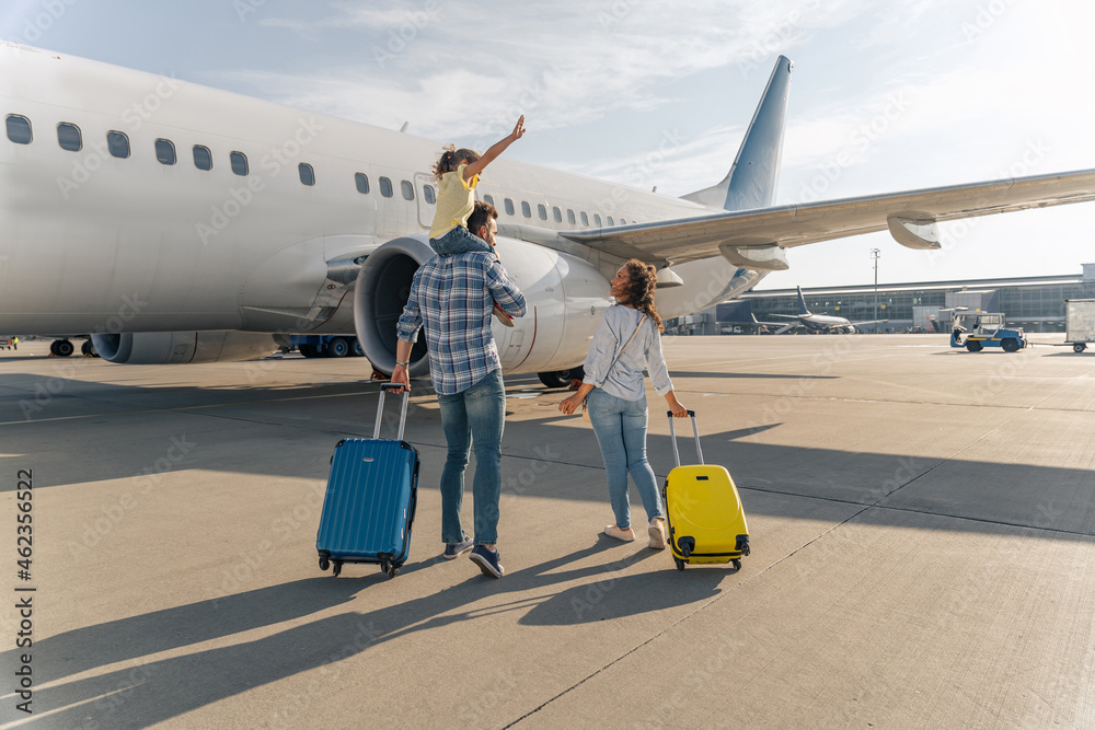幸福的一家人站在一架大飞机附近，带着两个行李箱。旅行概念