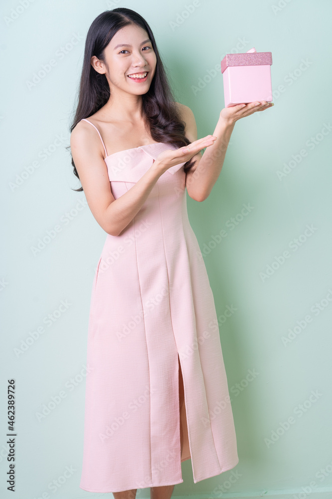 Beautiful young Asian woman holding pink gift box on green background