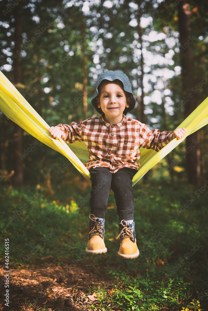 Small kid in yellow hammock in autumn forest. Childhood with pets concept