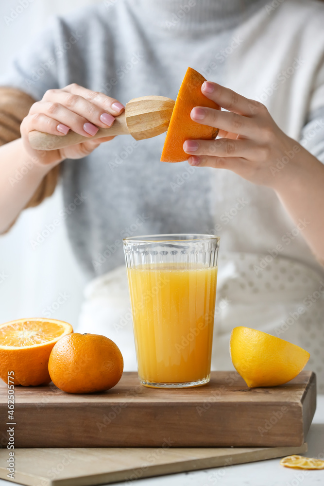 Woman making fresh citrus juice at table in kitchen