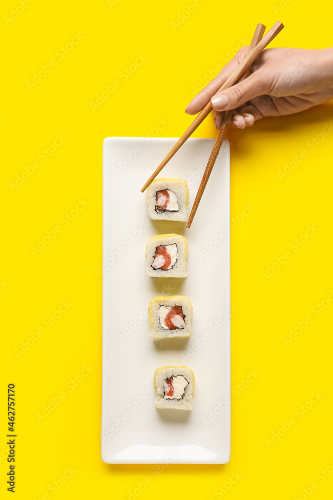 女人从黄色背景的盘子里拿美味的寿司卷