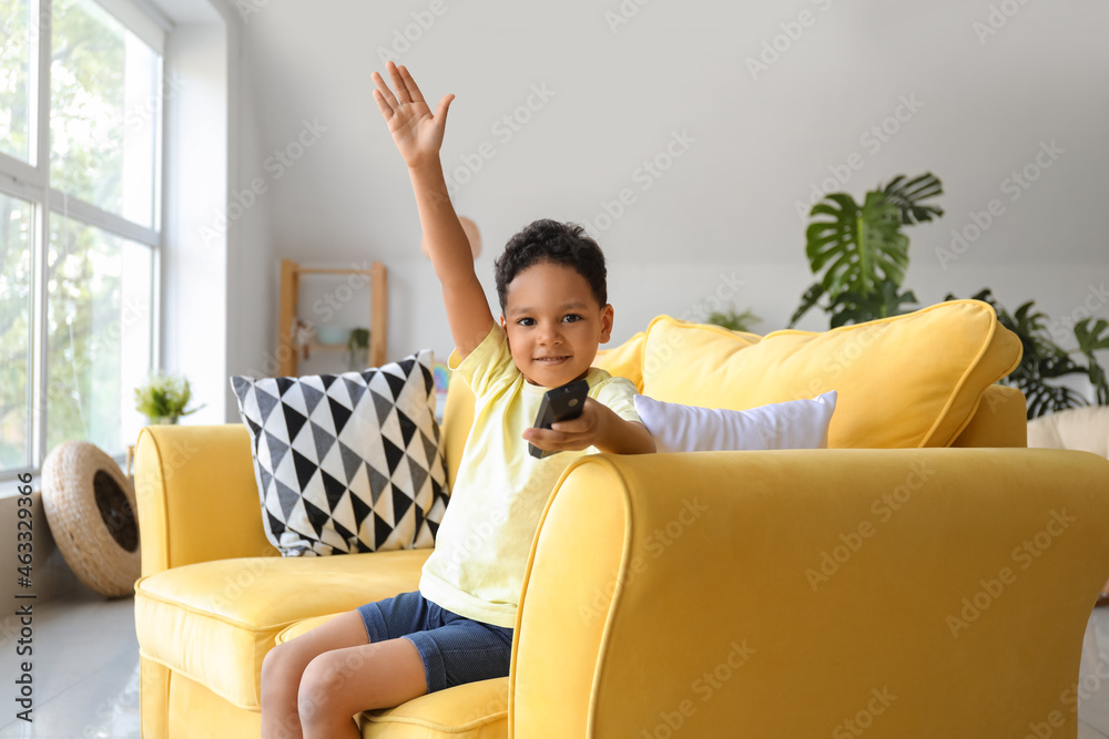 带着电视遥控器在家沙发上看动画片的非洲裔小男孩