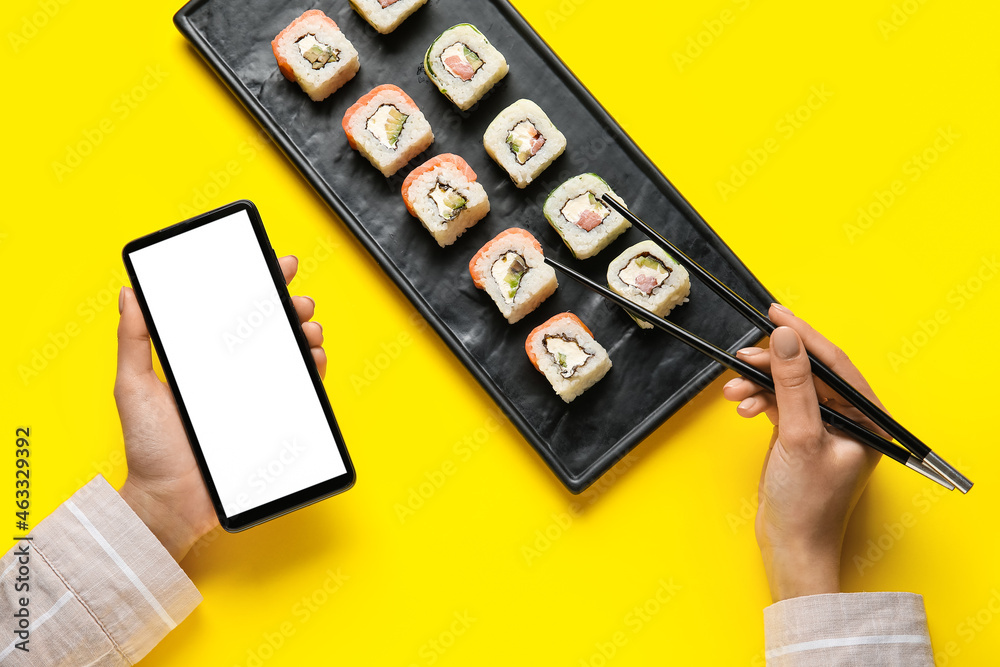 女人拿着手机，在彩色背景下吃美味的寿司卷