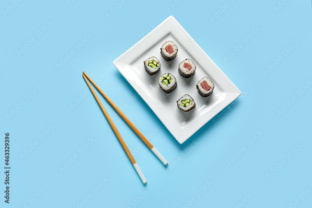 Plate with delicious maki rolls and wooden chopsticks on color background