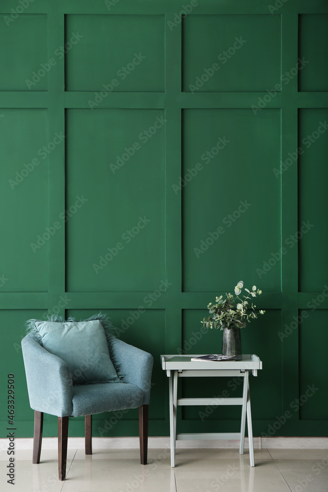 舒适的扶手椅和玻璃花瓶，绿色墙壁附近的桌子上有桉树