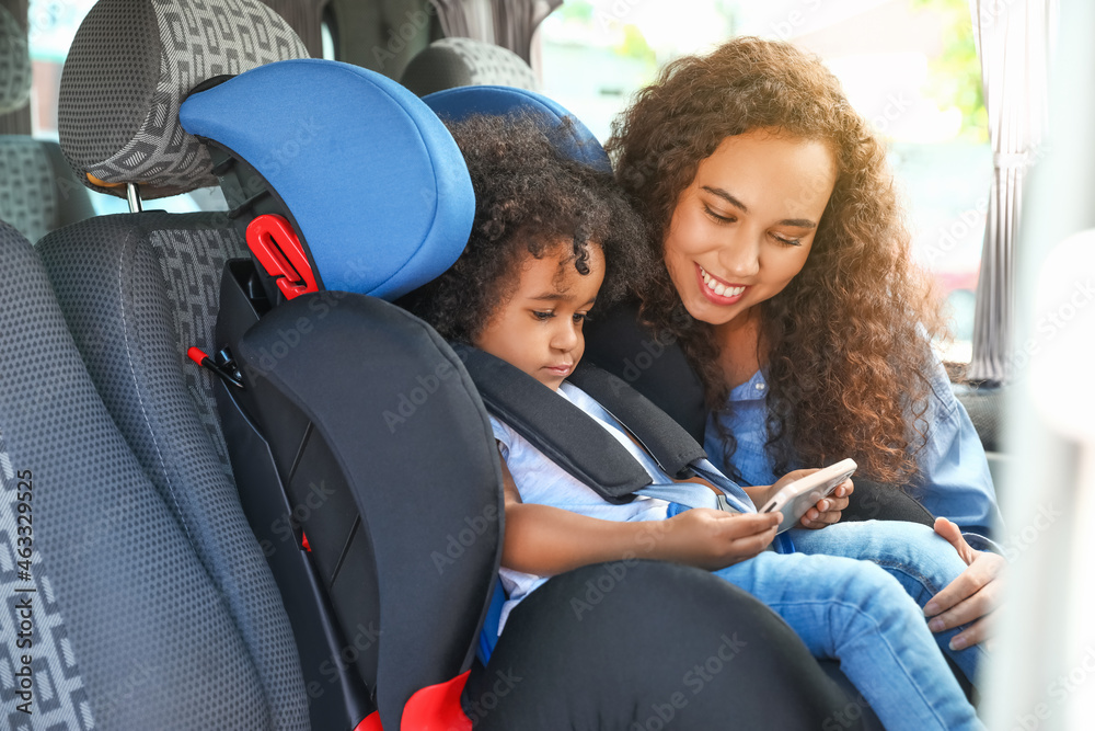 非裔美国妇女和她的小女儿在汽车安全座椅上看动画片