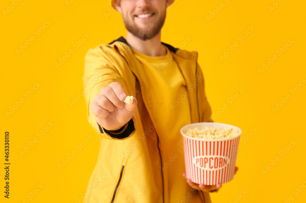 Smiling young man showing popcorn on color background