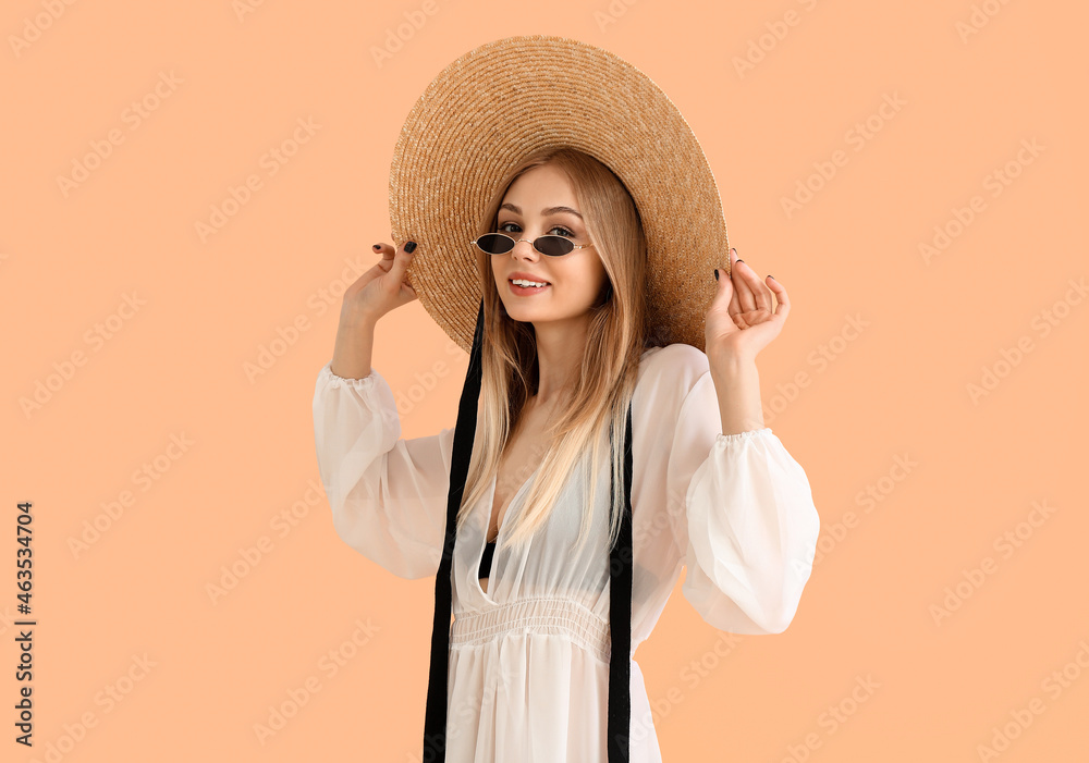 美丽微笑的女人穿着沙滩裙，触摸彩色背景上的柳条帽