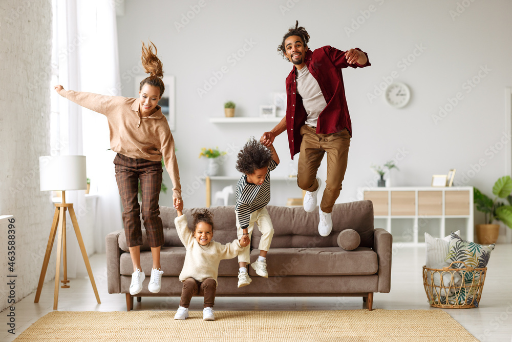 活跃的非洲裔美国年轻父母带着两个孩子在家里从沙发跳到地板上