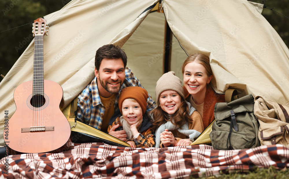 快乐的家庭父亲、母亲和两个小孩坐在森林露营地的帐篷里
