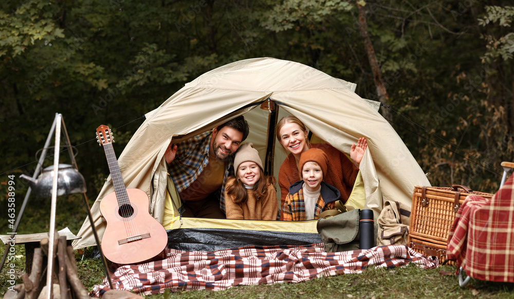 快乐的家庭父亲、母亲和两个小孩坐在森林露营地的帐篷里