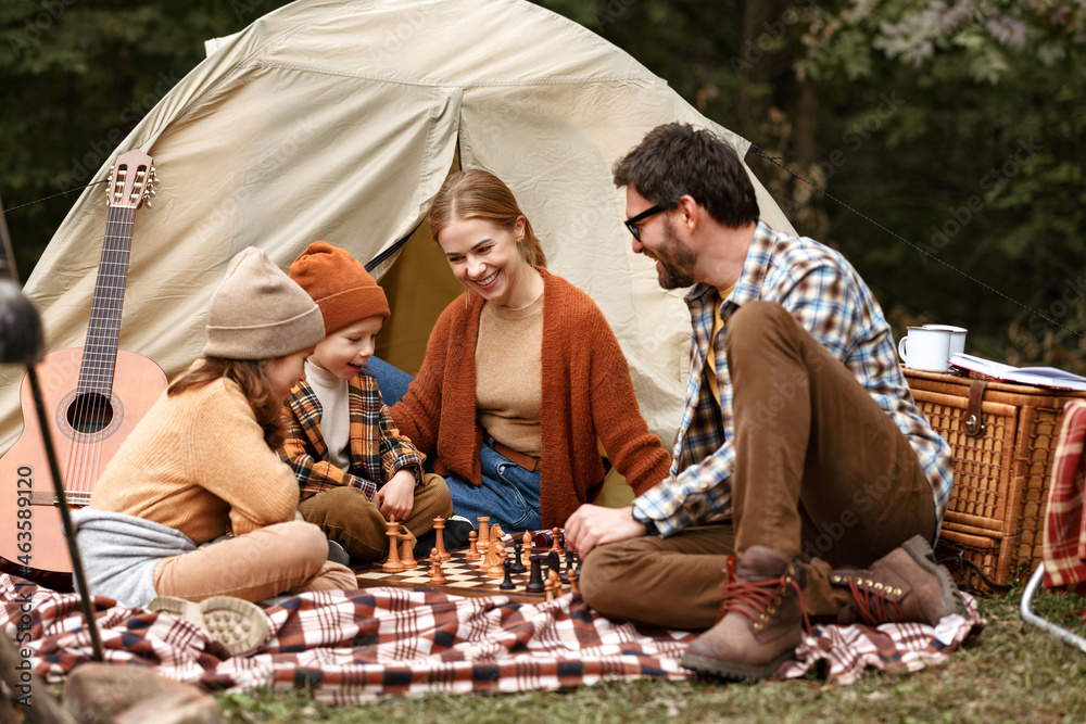 Happy smiling family playing chess game at campsite during camping trip in nature