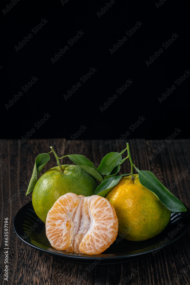 Fresh green tangerine on dark wooden table with black background.