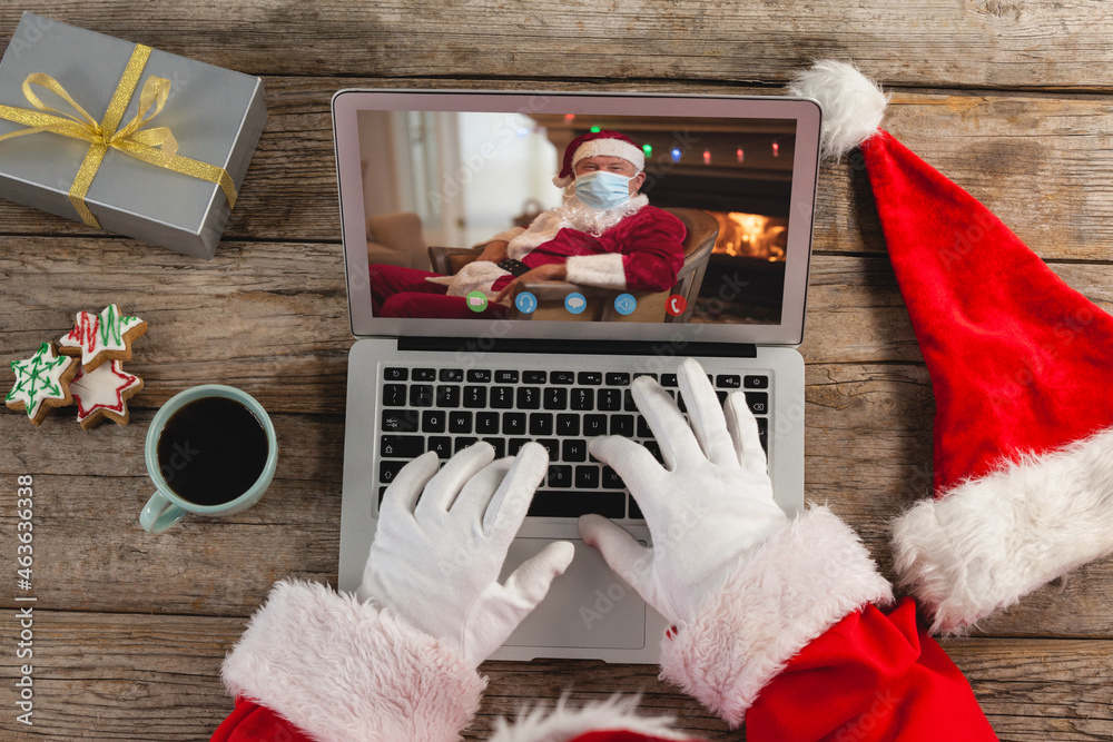 圣诞老人在圣诞笔记本电脑上与戴着口罩的高加索圣诞老人视频通话