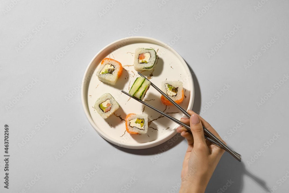 女人在浅色背景下从盘子里拿美味的寿司卷