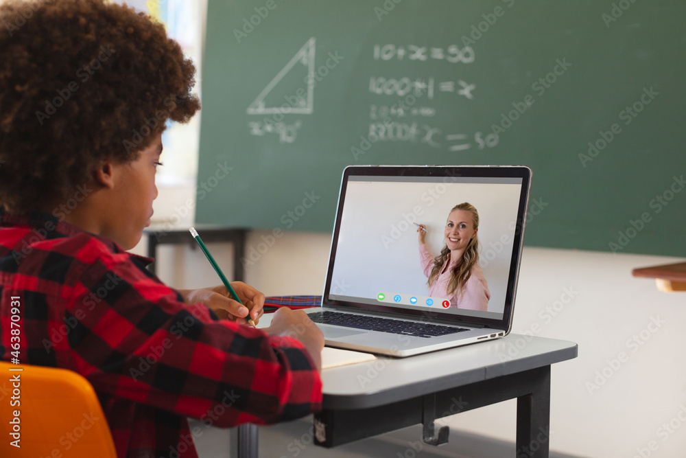 African american boy using laptop for video call, with smiling caucasian female teacher on screen