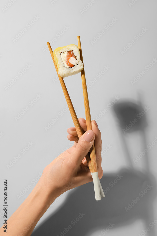 拿着木筷子的女人，浅色背景上有美味的寿司卷