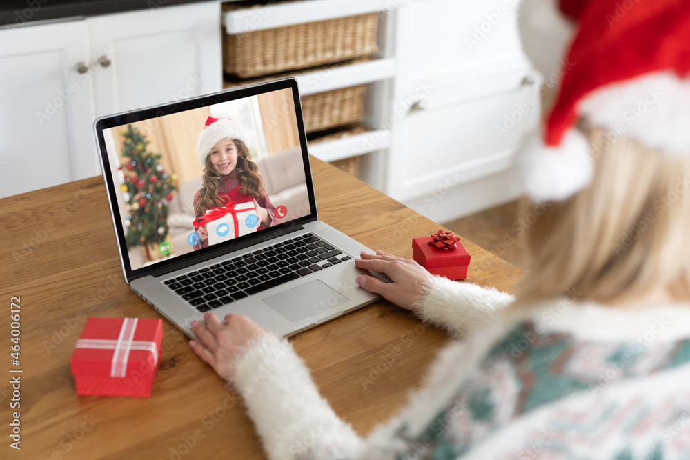 戴圣诞老人帽的白人妇女在圣诞笔记本电脑上与女性朋友视频通话