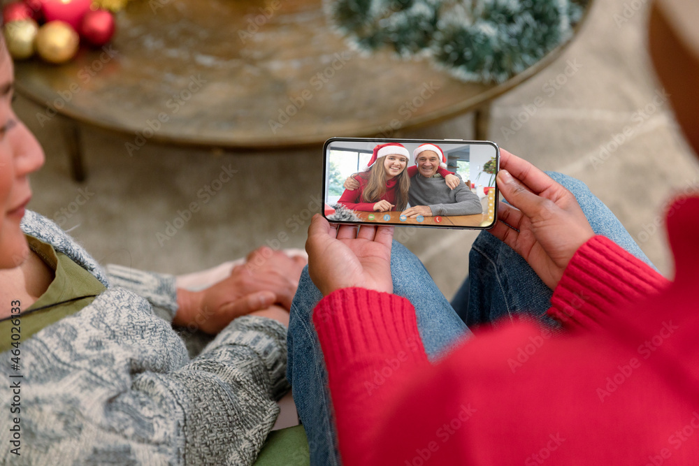 微笑的多元化夫妇与拥抱的高加索夫妇进行智能手机圣诞视频通话
