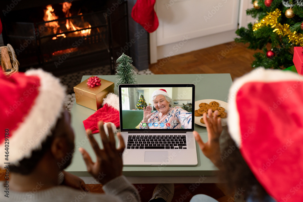 African american couple in santa hats on christmas video call with senior female friend