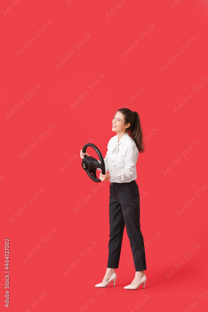 Young businesswoman with steering wheel on red background