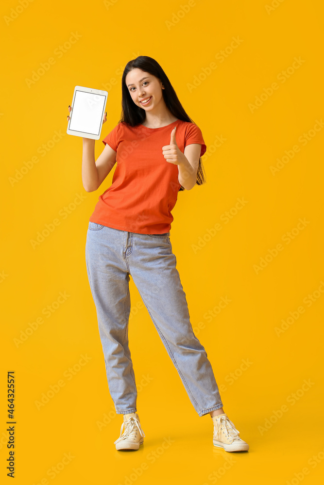 漂亮的十几岁女孩，平板电脑在黄色背景上显示拇指向上