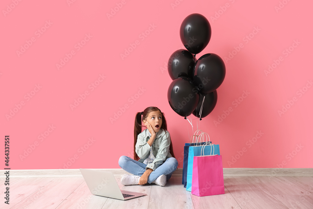 震惊的小女孩在粉色墙上拿着笔记本电脑。黑色星期五大减价