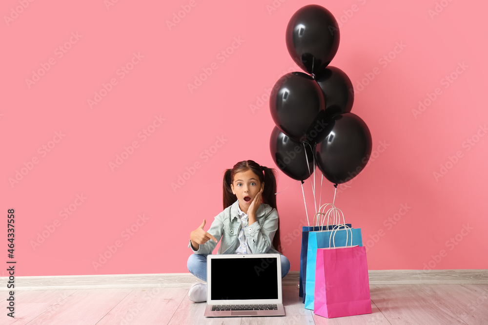 震惊的小女孩指着粉色墙上的笔记本电脑。黑色星期五大减价