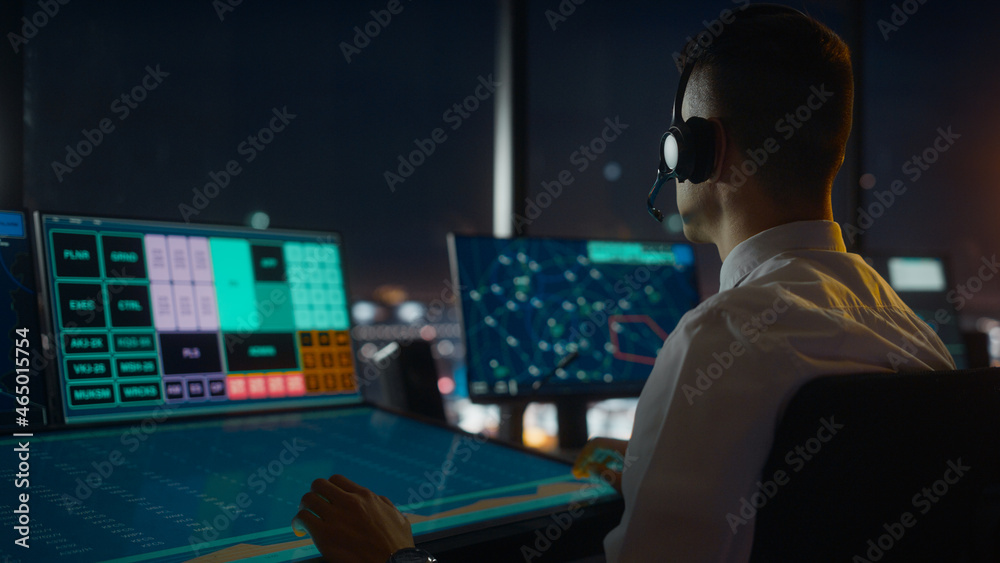 Male Air Traffic Controller with Headset Talk on a Call in Airport Tower. Office Room is Full of Des